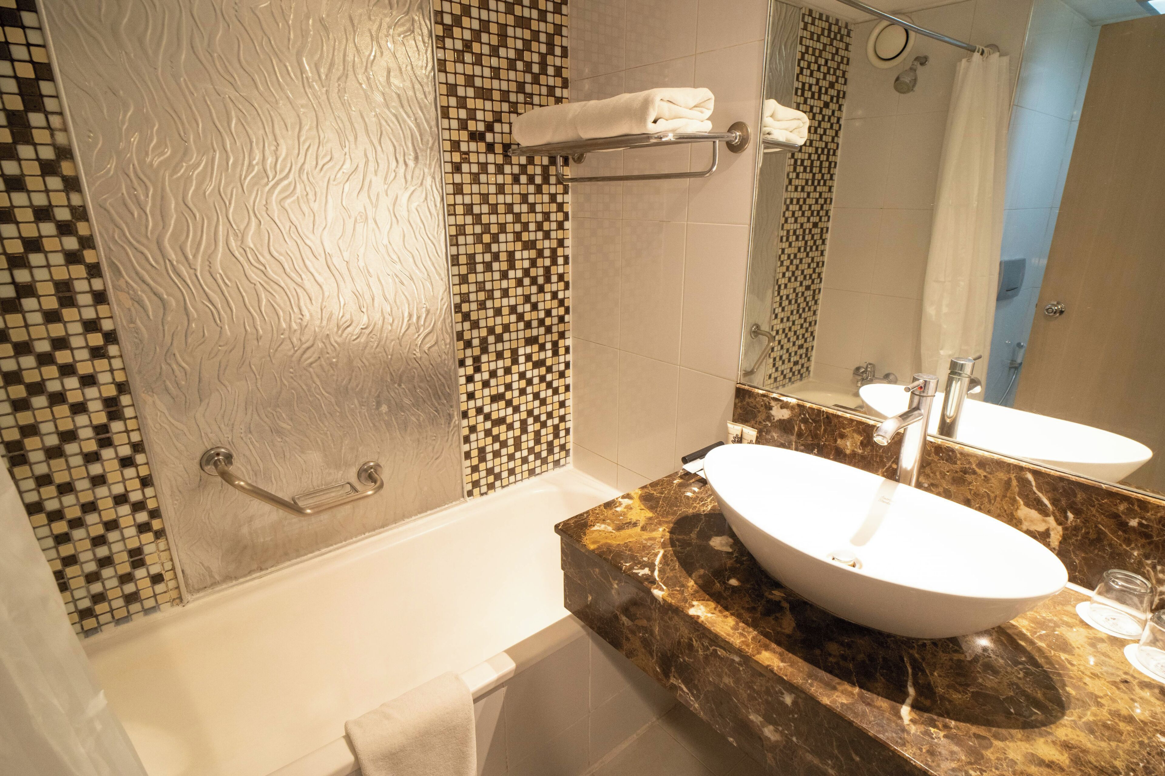 A bathroom with a bathtub, a white sink, a mirror, and a shower curtain.