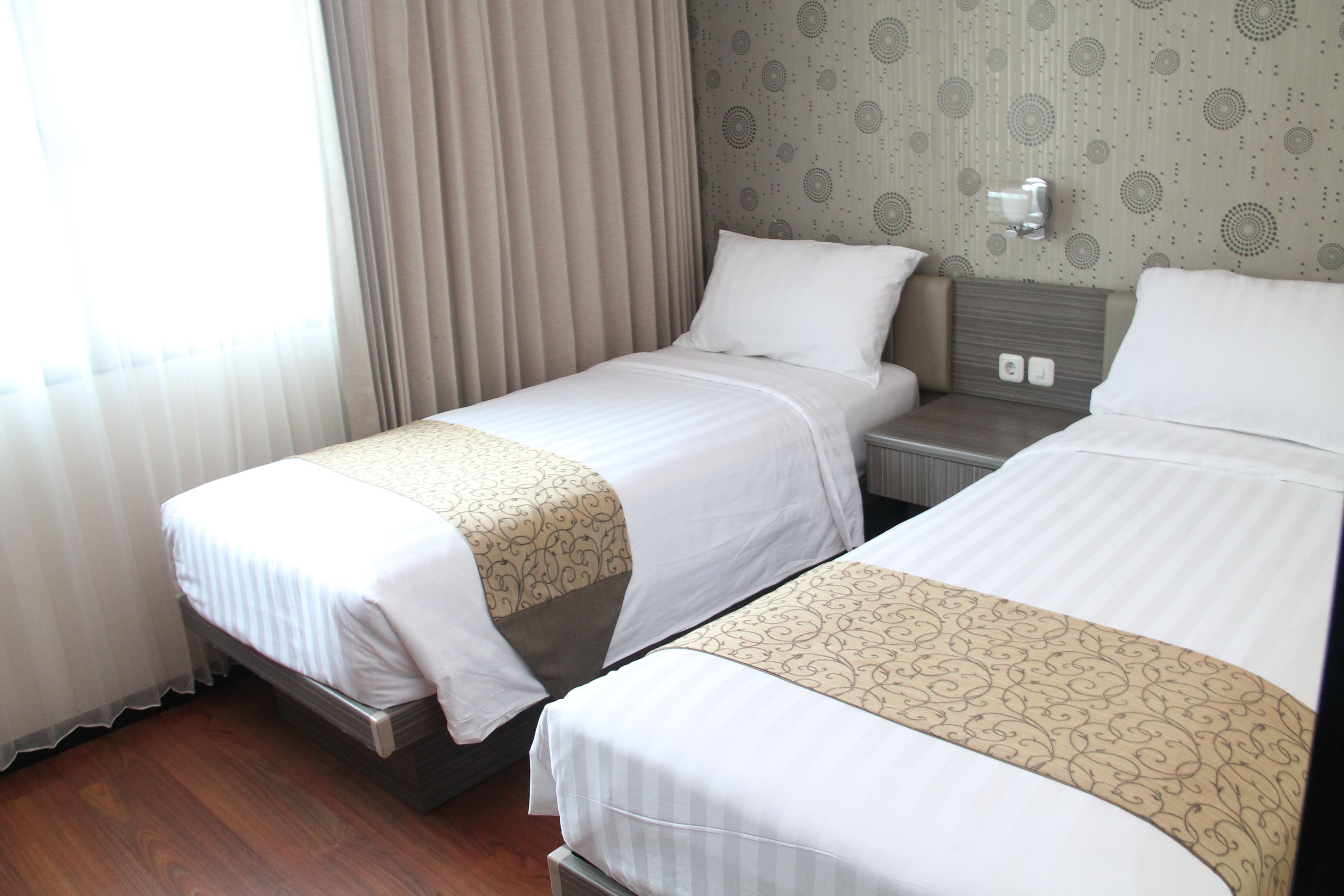 Una habitación de hotel con dos camas, piso de madera y una ventana con cortinas.