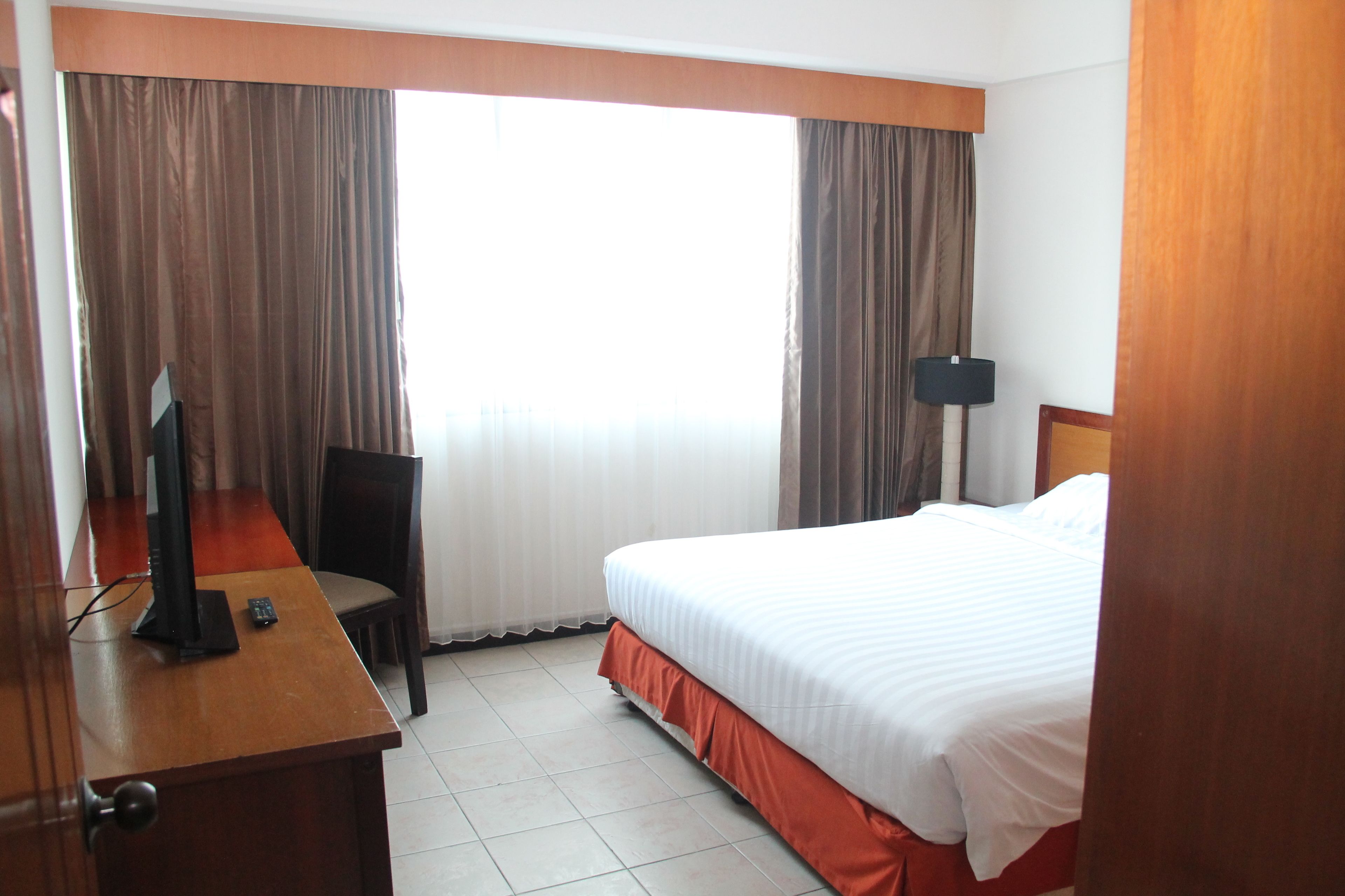 Une chambre d’hôtel avec un lit, un bureau équipé d’un ordinateur, une chaise et une lampe.