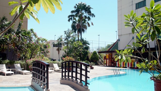 Une piscine avec un pont, des chaises longues et des plantes en pot.