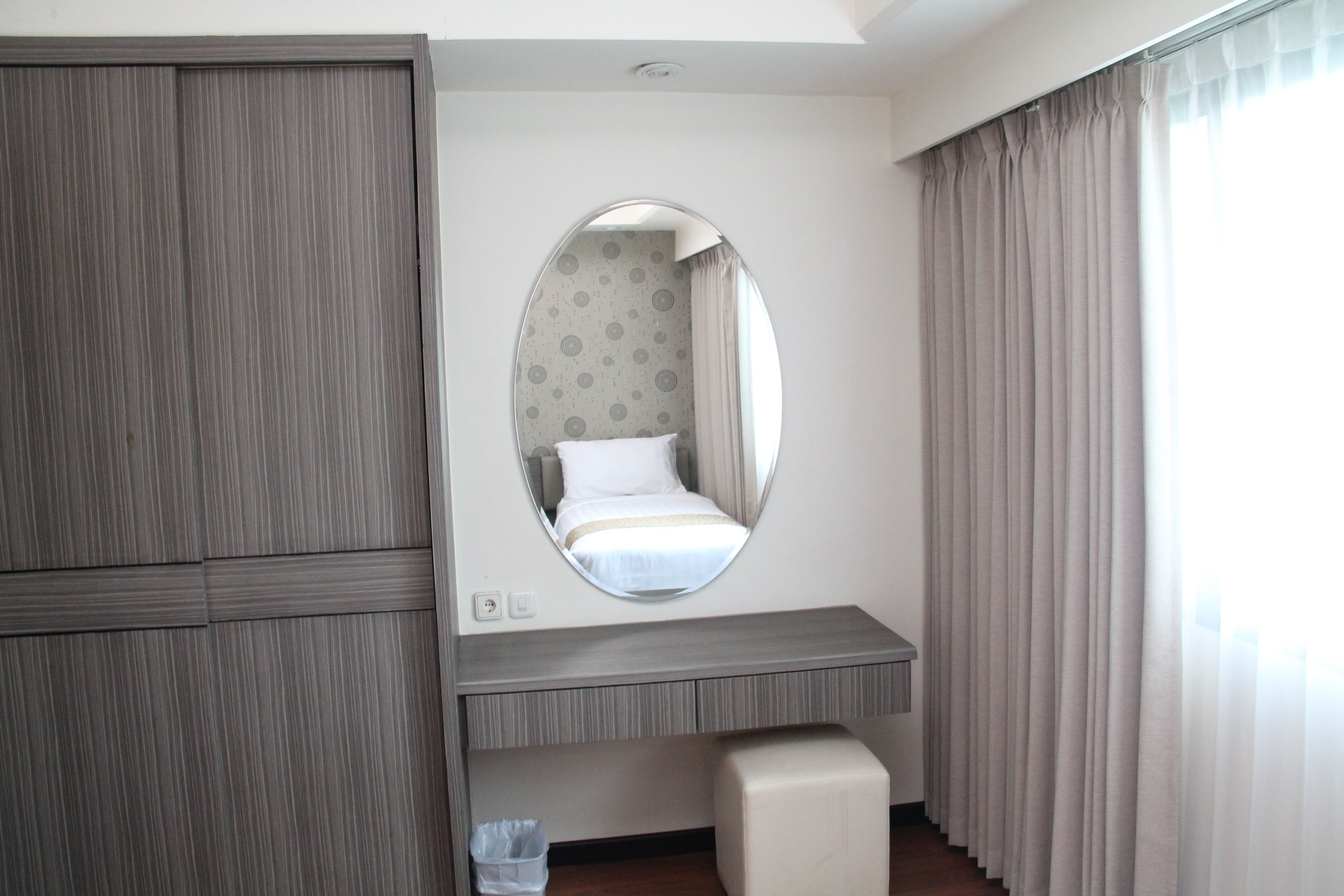 A hotel room with a bed, a mirror, a desk, and a trash bin.