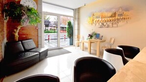 A modern hotel lobby with a large window, a black leather sofa, a wooden table, and a mural of a historical building. - Kracow Residence Hotel (Krakow)