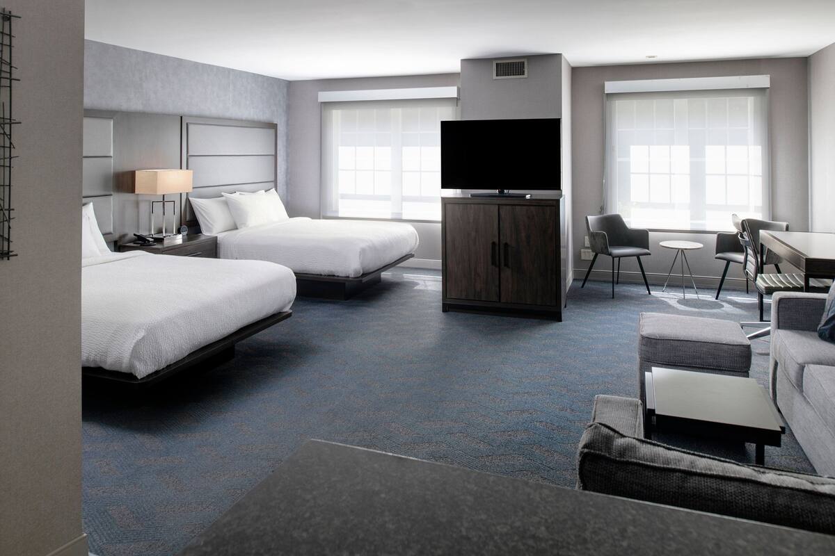 A modern hotel room with two beds, a TV, a desk, and a sofa.