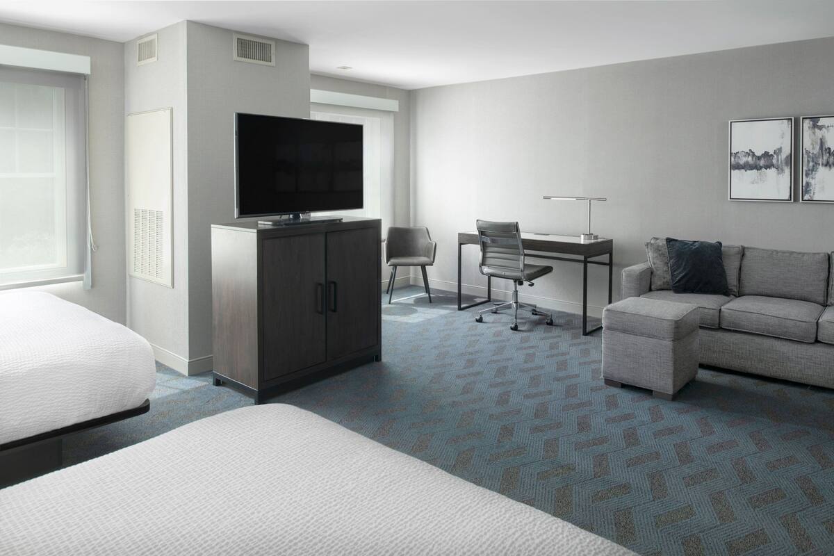 A hotel room with a bed, a desk, a chair, a sofa, and a television.