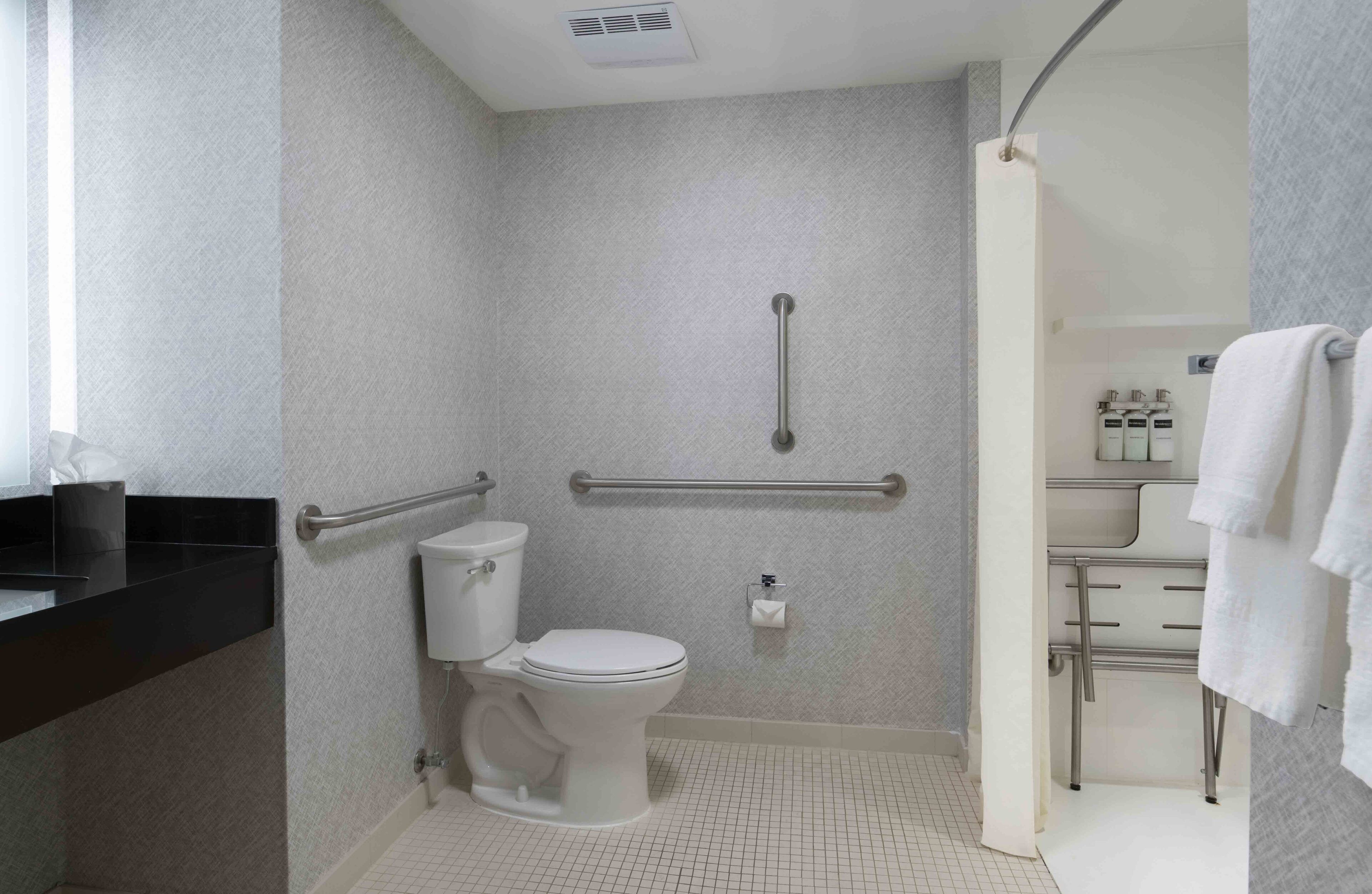 A bathroom with a white toilet, a handrail, and a sink area with towels.