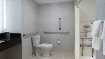 A bathroom with a white toilet, a handrail, and a sink area with towels.