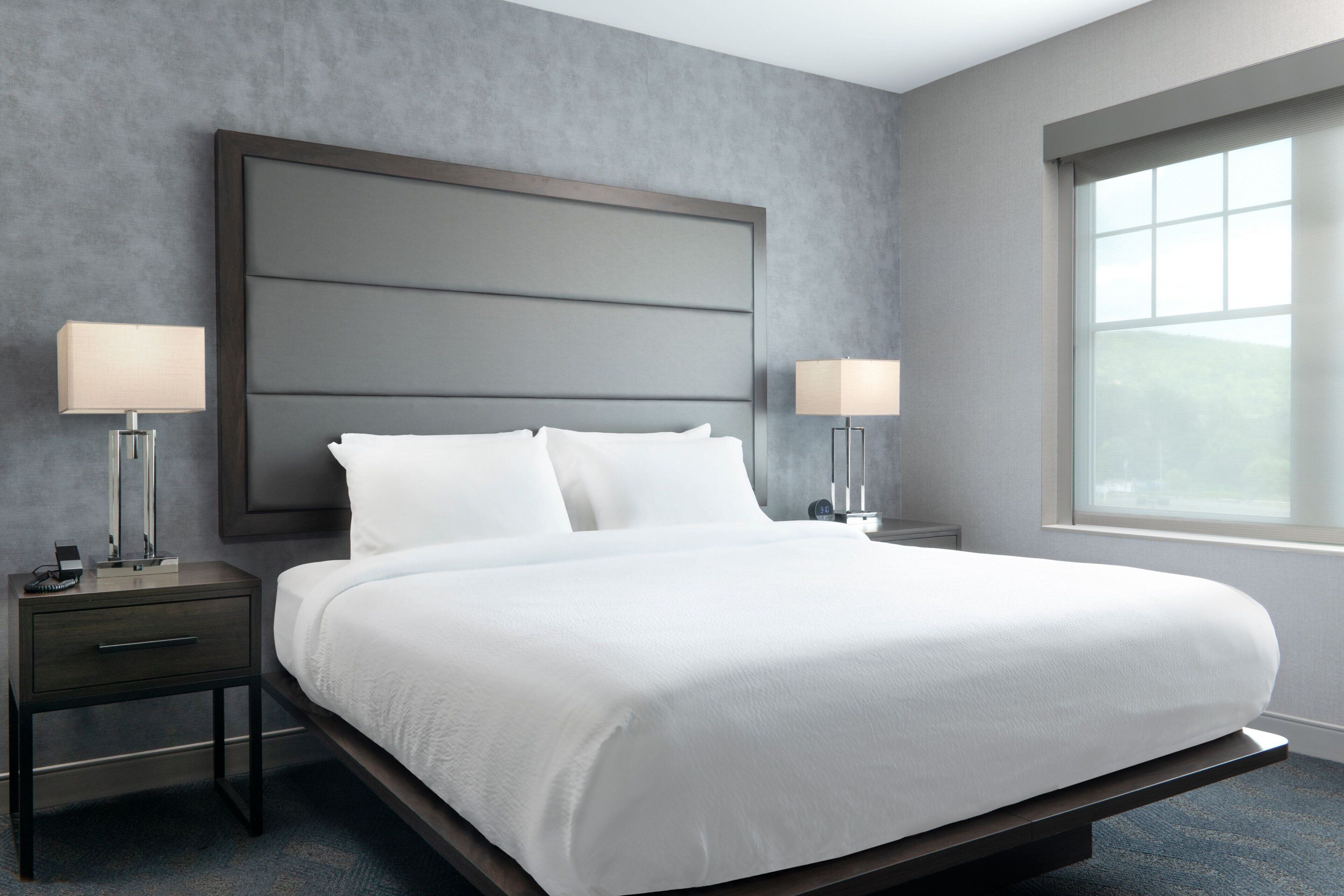 A modern hotel room with a large bed, two bedside tables, and a window with a view.