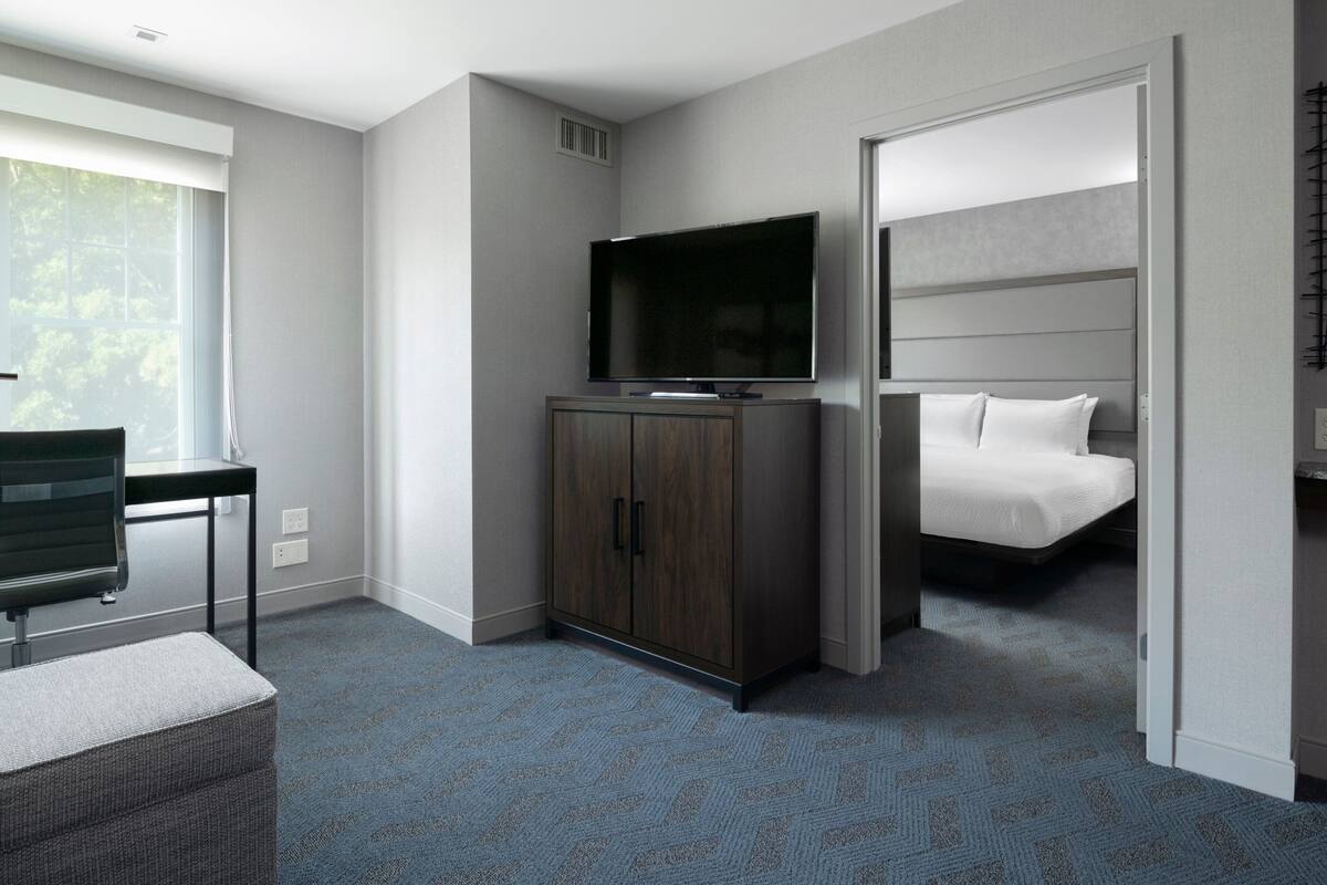A hotel room with a bed, a television on a cabinet, a desk, and a chair.