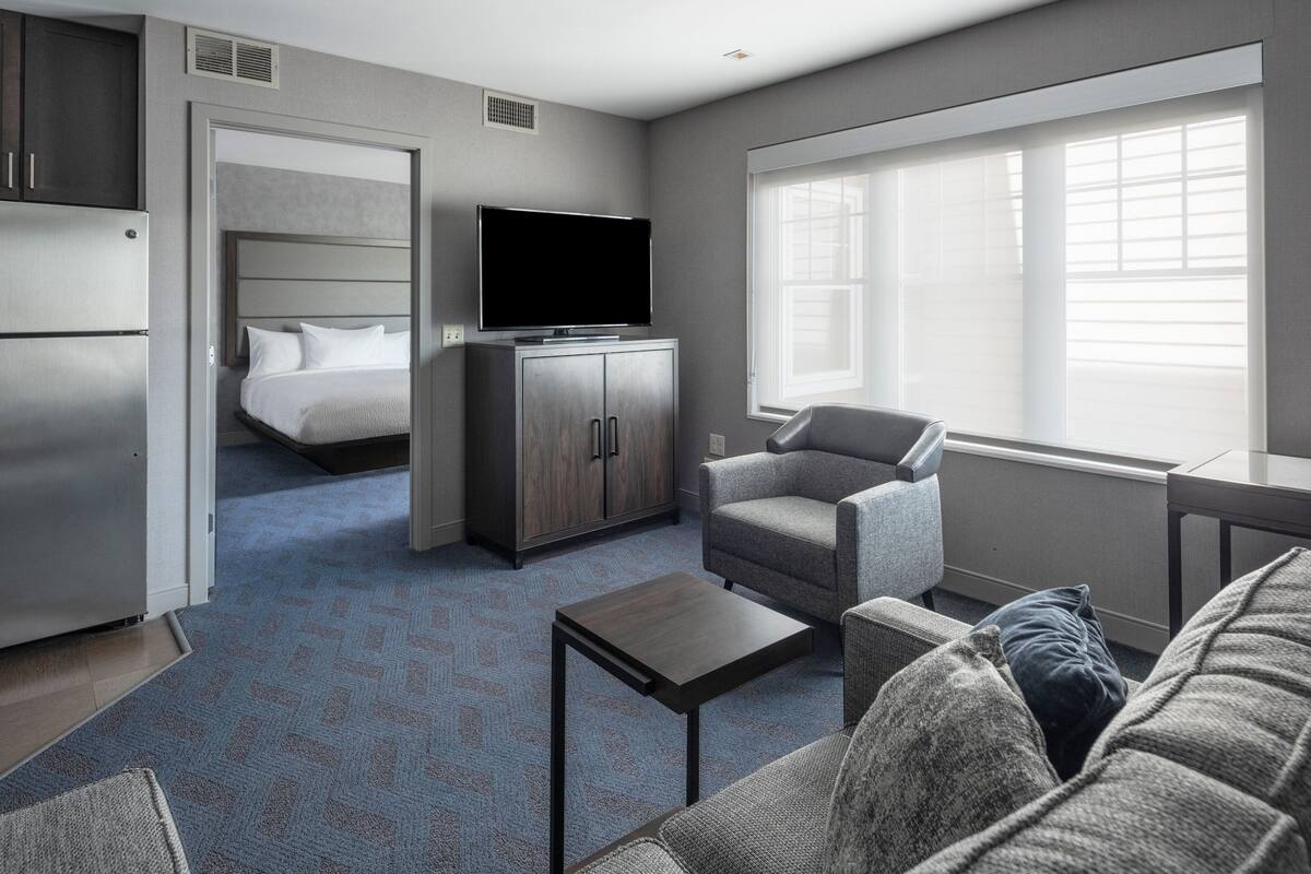 A hotel room with a bed, a TV, a sofa, a coffee table, and a window with blinds.