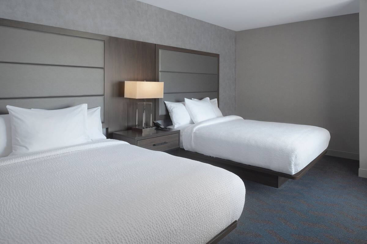 A hotel room with two beds, a nightstand with a lamp, and a large headboard.