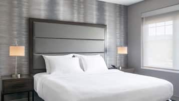 A modern hotel room with a large bed, two bedside tables with lamps, and a large window providing natural light.
