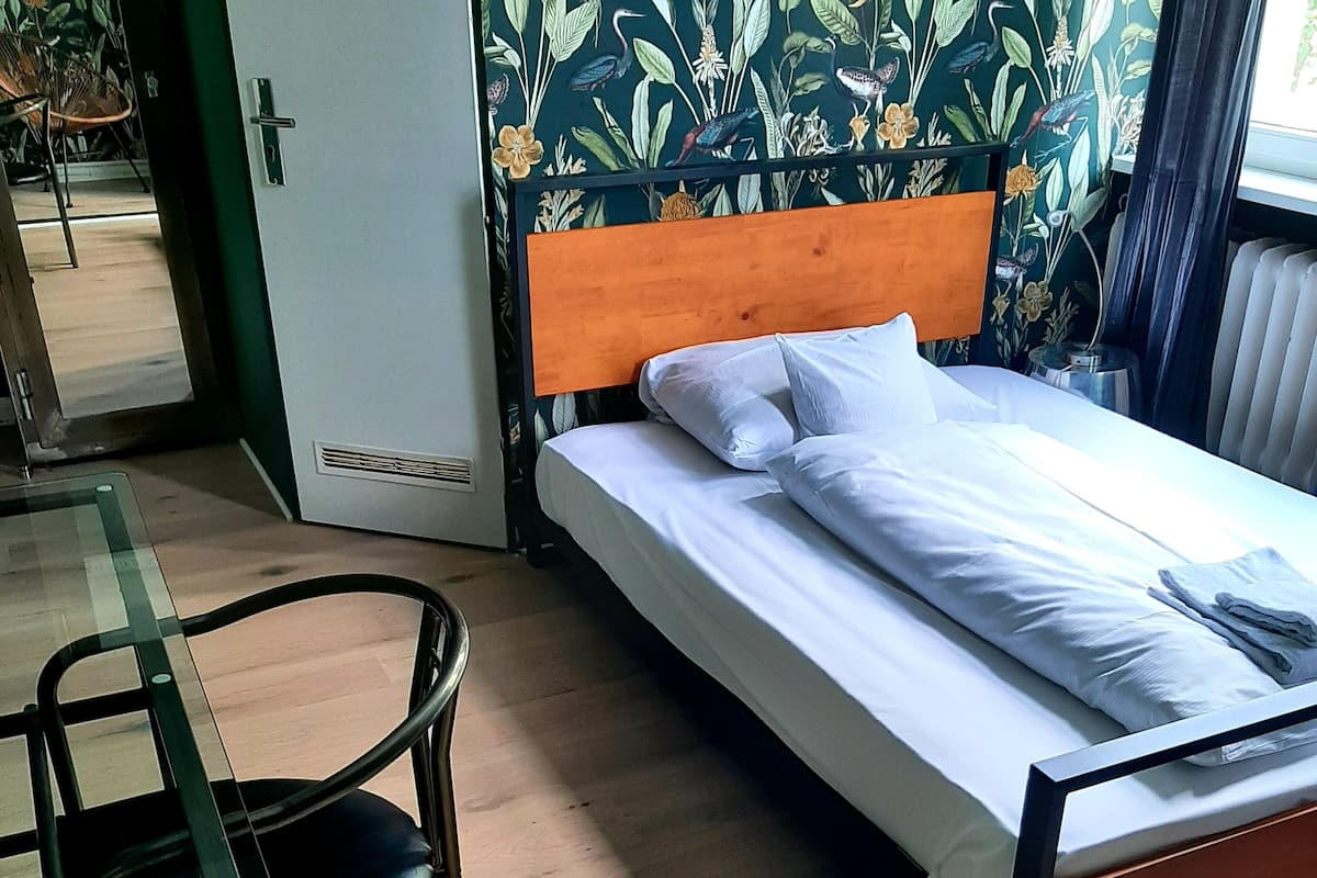 A single bed with white linens in a room with a wooden floor and a floral wallpaper headboard.