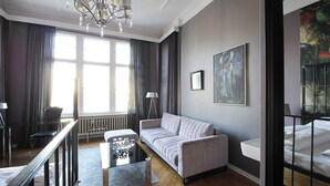 Un salon moderne avec un canapé, une table basse et un lustre. Il y a une fenêtre avec des rideaux et un radiateur.