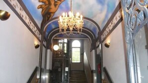 Un magnifique escalier orné de balustrades travaillées et surmonté d’un lustre, menant à une porte dotée d’un panneau de verre.