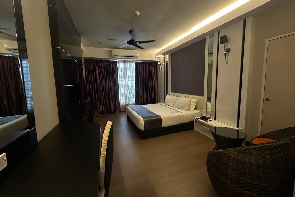 A modern hotel room with a bed, a desk, a chair, a ceiling fan, and a large window with curtains.