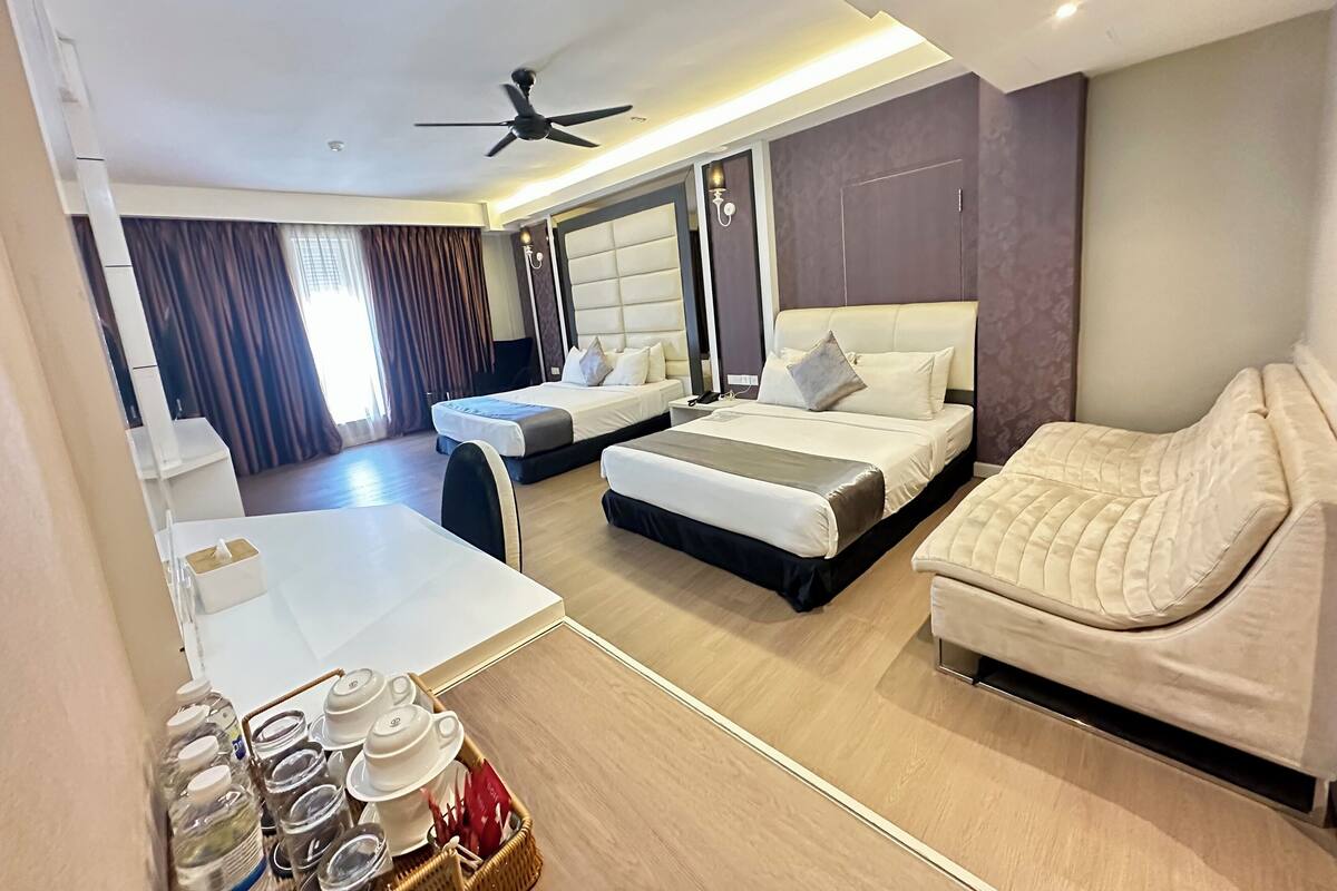 A hotel room with two beds, a sofa, a dining table, and a ceiling fan.