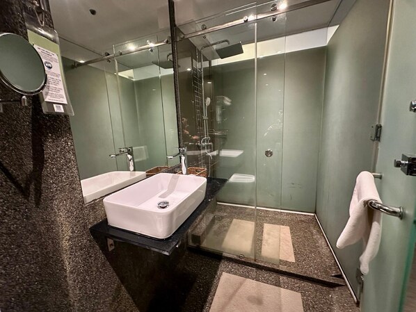 Un baño moderno con ducha envuelta en vidrio, un lavamanos blanco y un espejo.