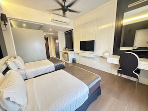 Ein Hotelzimmer mit zwei Betten, einem Schreibtisch, einem Sessel, einem Fernseher und einem Deckenventilator.