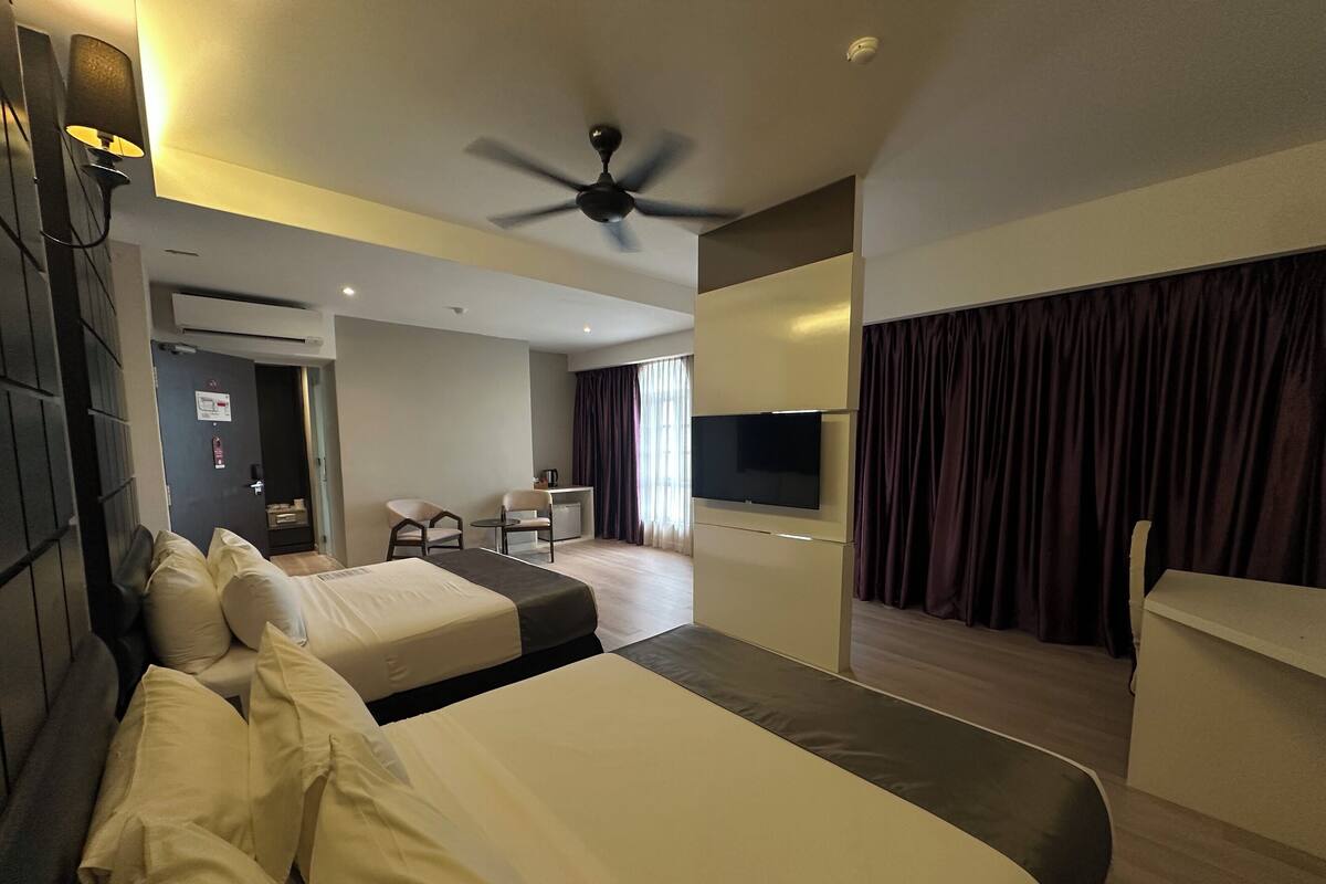 A hotel room with two beds, a desk, a television, and a ceiling fan.