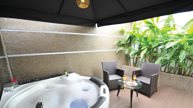 A spa area with a hot tub, wicker chairs, a glass table, and tropical plants. - The Sterling (Malacca City)