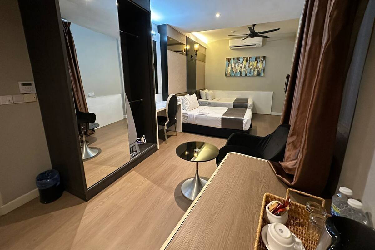 A hotel room with a bed, a desk, a chair, a small table, a mirror, and a ceiling fan.