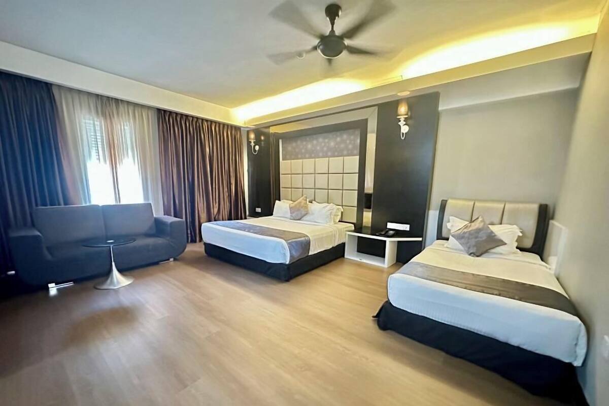 A hotel room with two beds, a sofa, a small table, and a ceiling fan.