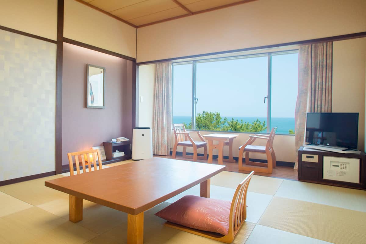 A traditional Japanese-style room with tatami flooring, a low wooden table, and a television on a cabinet.