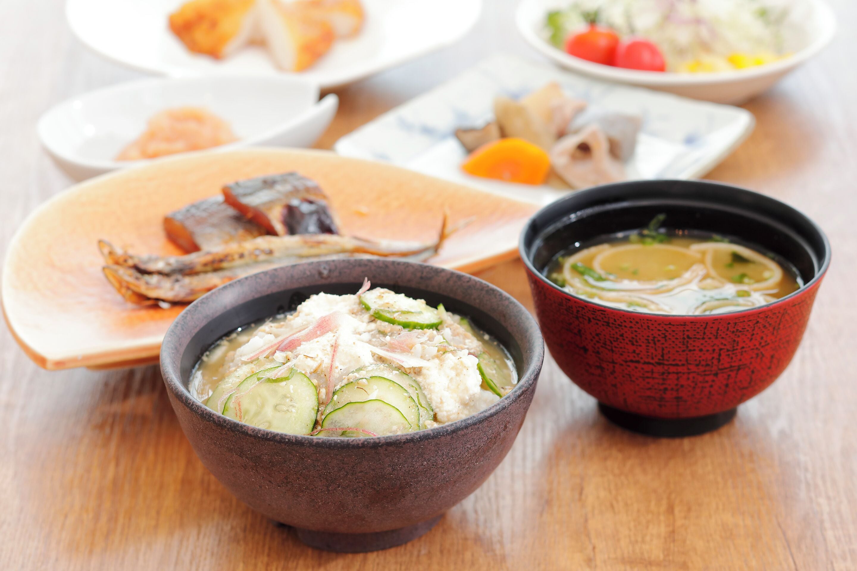 A table with various dishes including a bowl of soup, a plate with fish, and other food items.