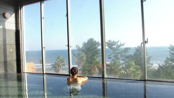 A person sitting by a large window overlooking a beach.