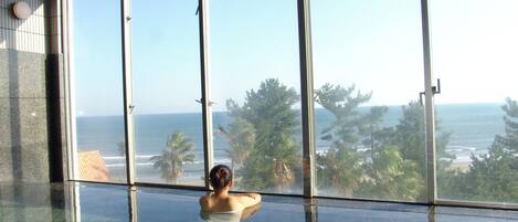 A person sitting by a large window overlooking a beach.