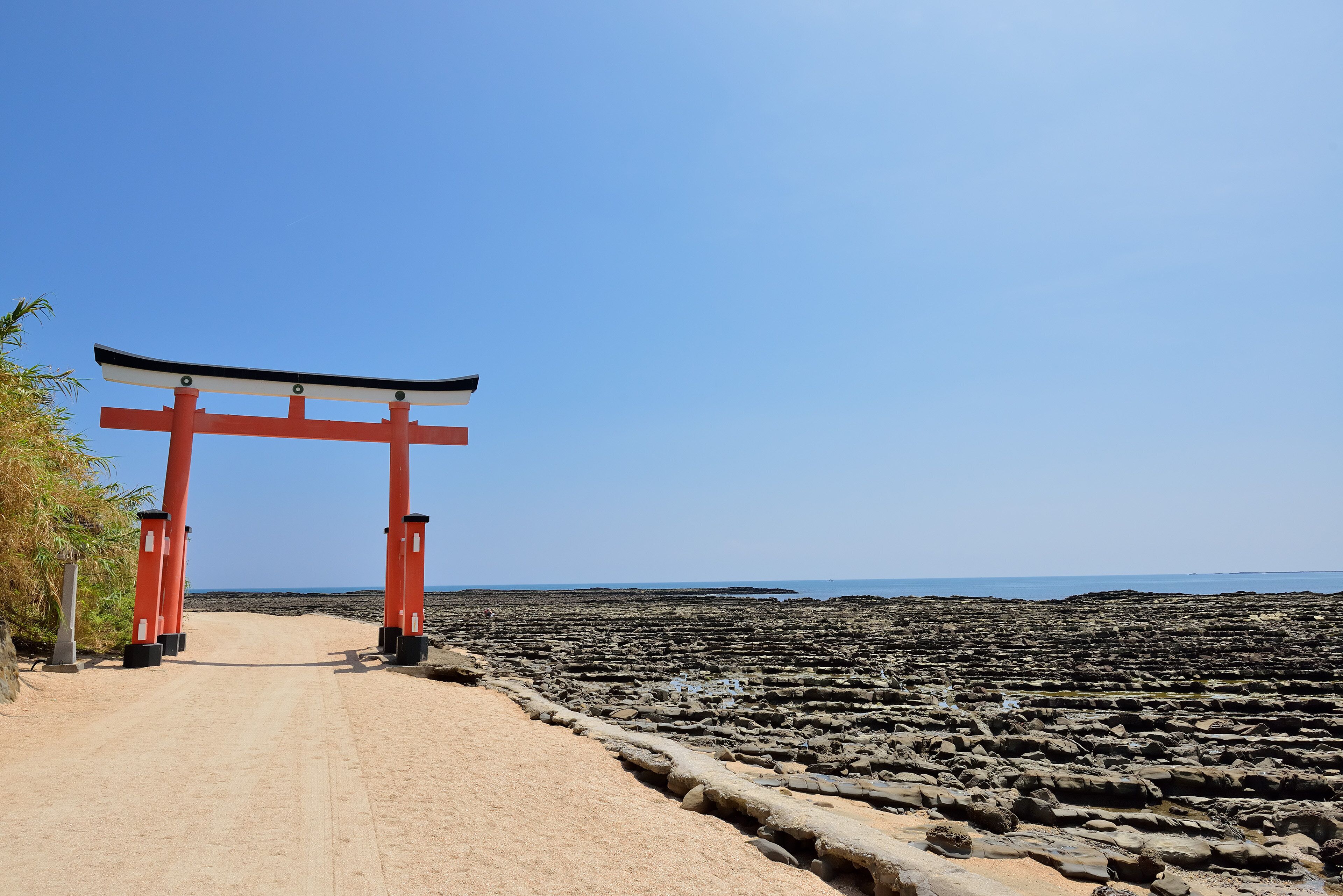 Un torii japonés tradicional a la entrada de una playa rocosa.
