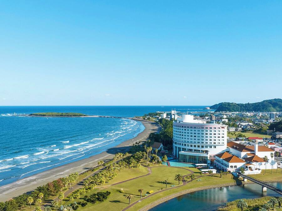A coastal hotel with a beachfront view, a swimming pool, and a bridge connecting to the mainland.
