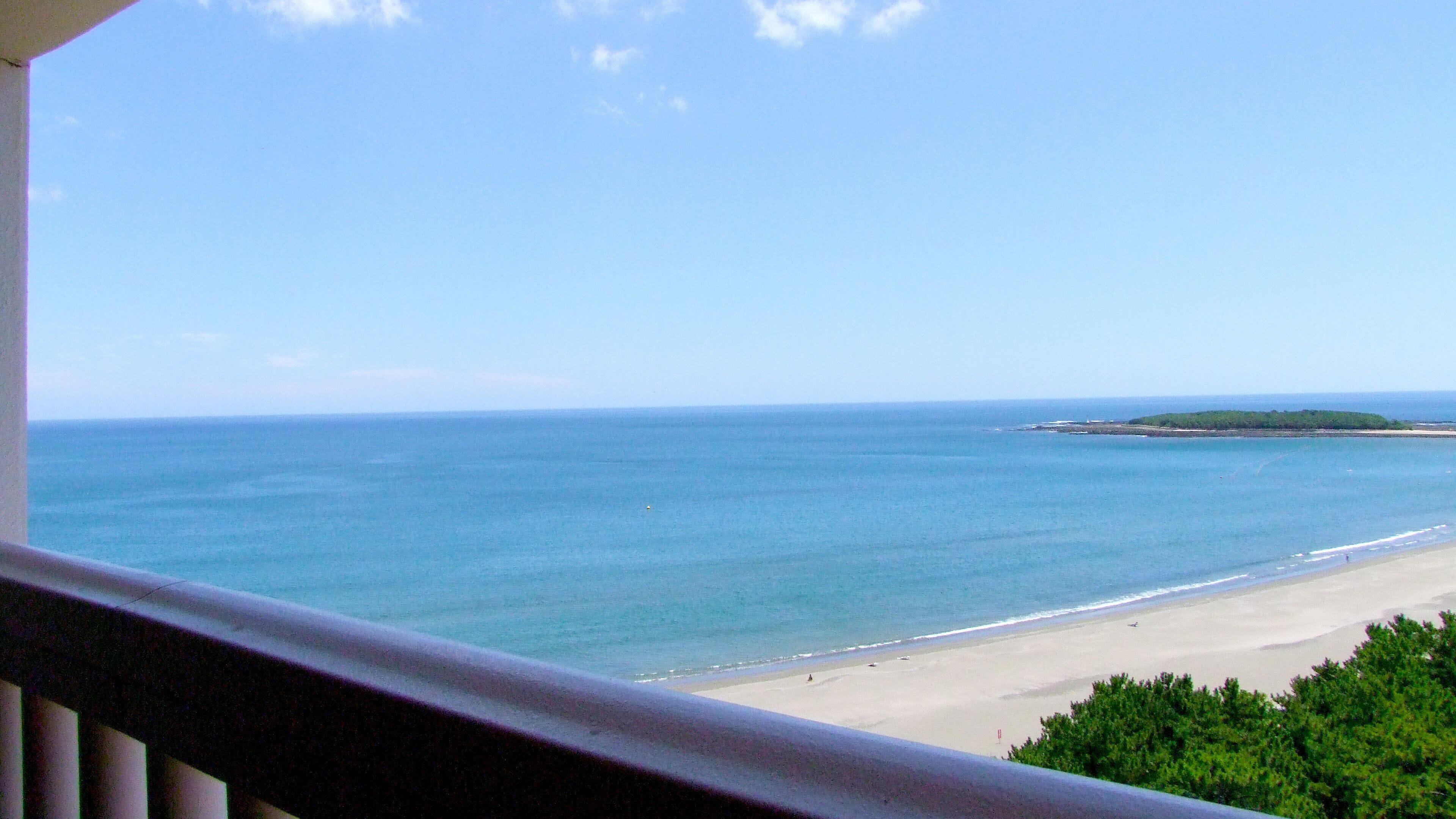 Blick auf einen Strand mit blauem Himmel und ruhigem Wasser.