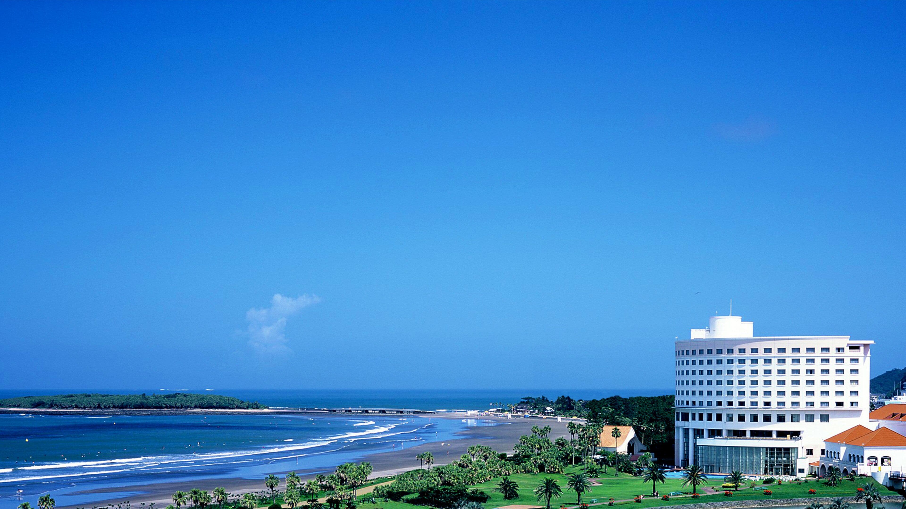 A coastal hotel with a beach view, a large building with multiple floors, and a well-maintained lawn.