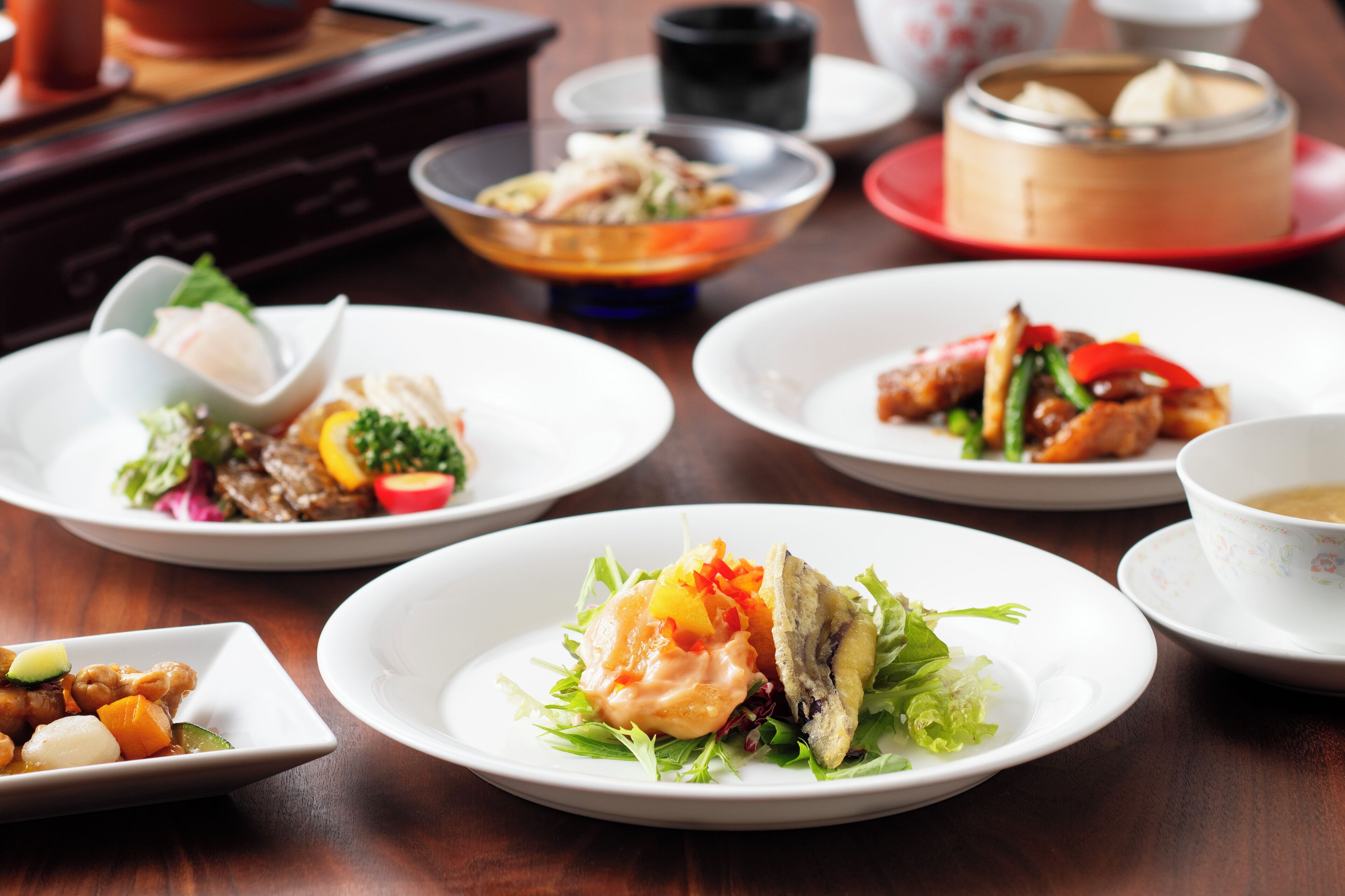 Una variedad de platos sobre una mesa de madera, incluyendo un tazón de sopa, un plato con ensalada y un plato con pescado.