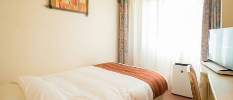 Una habitación de hotel con una cama, televisión y una ventana con cortinas.
