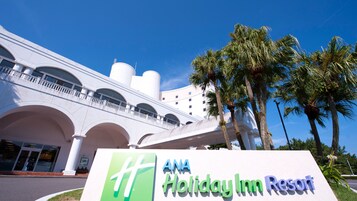 A hotel with a sign reading 'ANA Holiday Inn Resort' and a white building with arched windows and a balcony.
