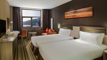 Habitación de hotel con dos camas, un escritorio, una silla, una ventana con vistas a un paisaje nevado y un cuadro en la pared.