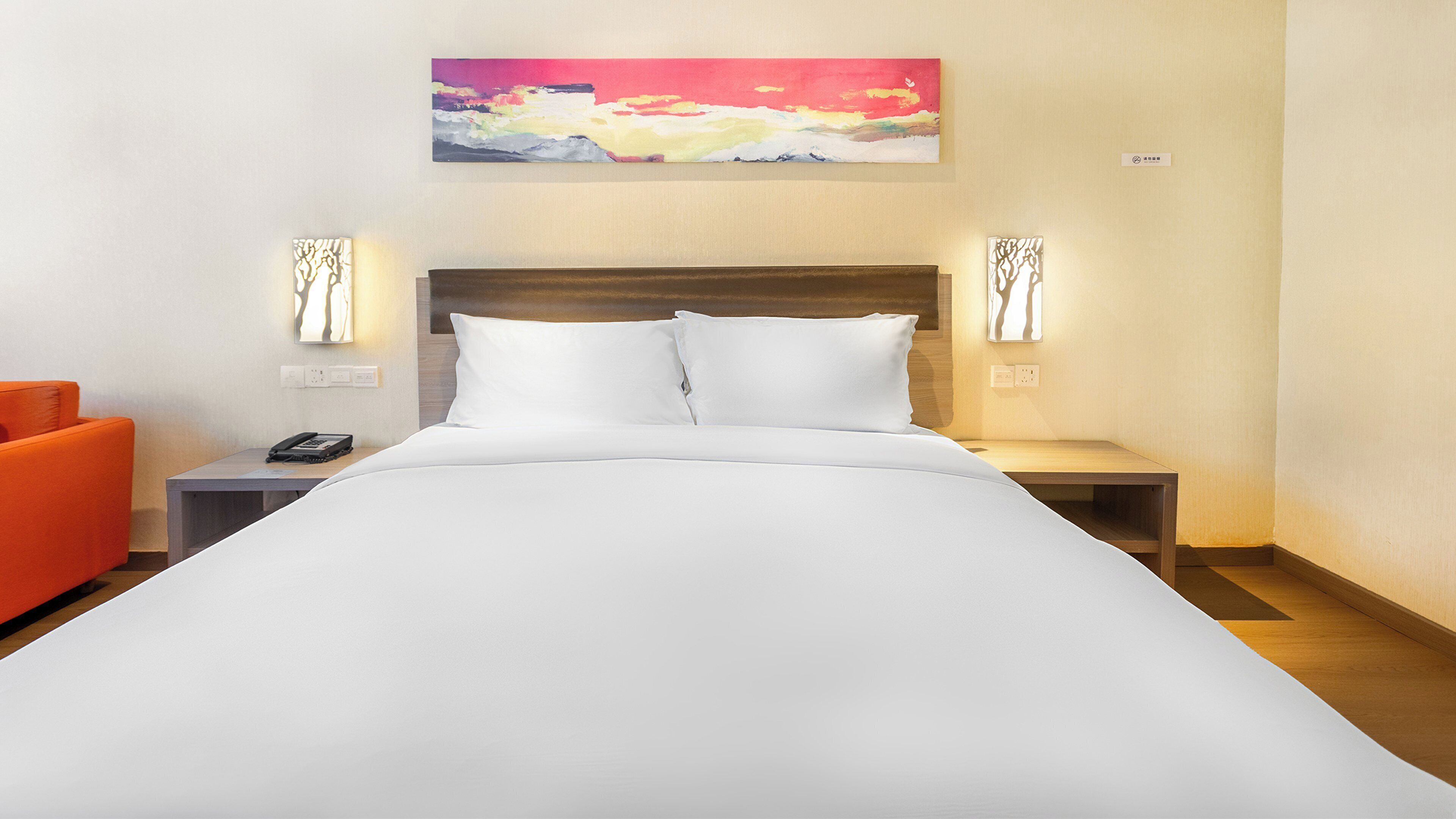 A hotel room with a large bed, two bedside tables, a nightstand, a chair, and a painting on the wall.