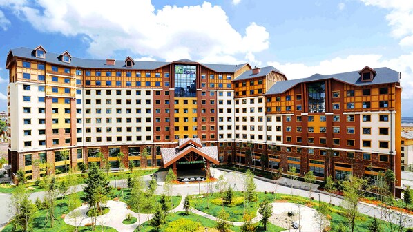 A multi-story hotel with a central atrium, surrounded by landscaped gardens and a parking area.