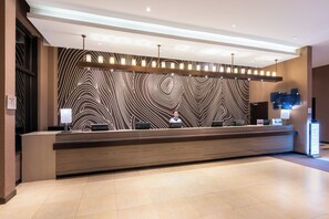 A reception desk with a modern design, a patterned wall, and a clean, tiled floor. - Holiday Inn Express Changbaishan by IHG (Baishan)