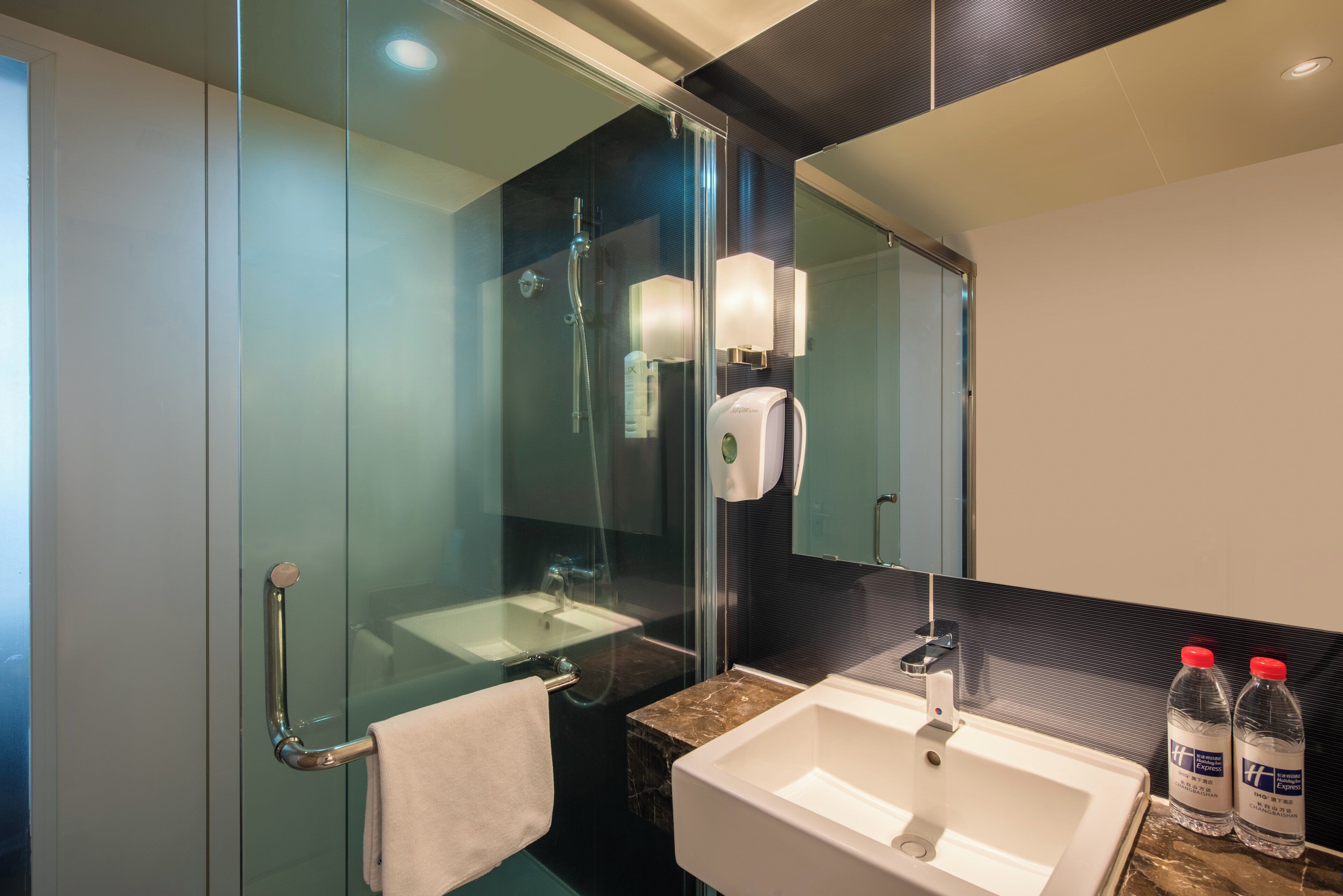 A modern bathroom with a glass shower enclosure, a white sink, and a marble countertop.