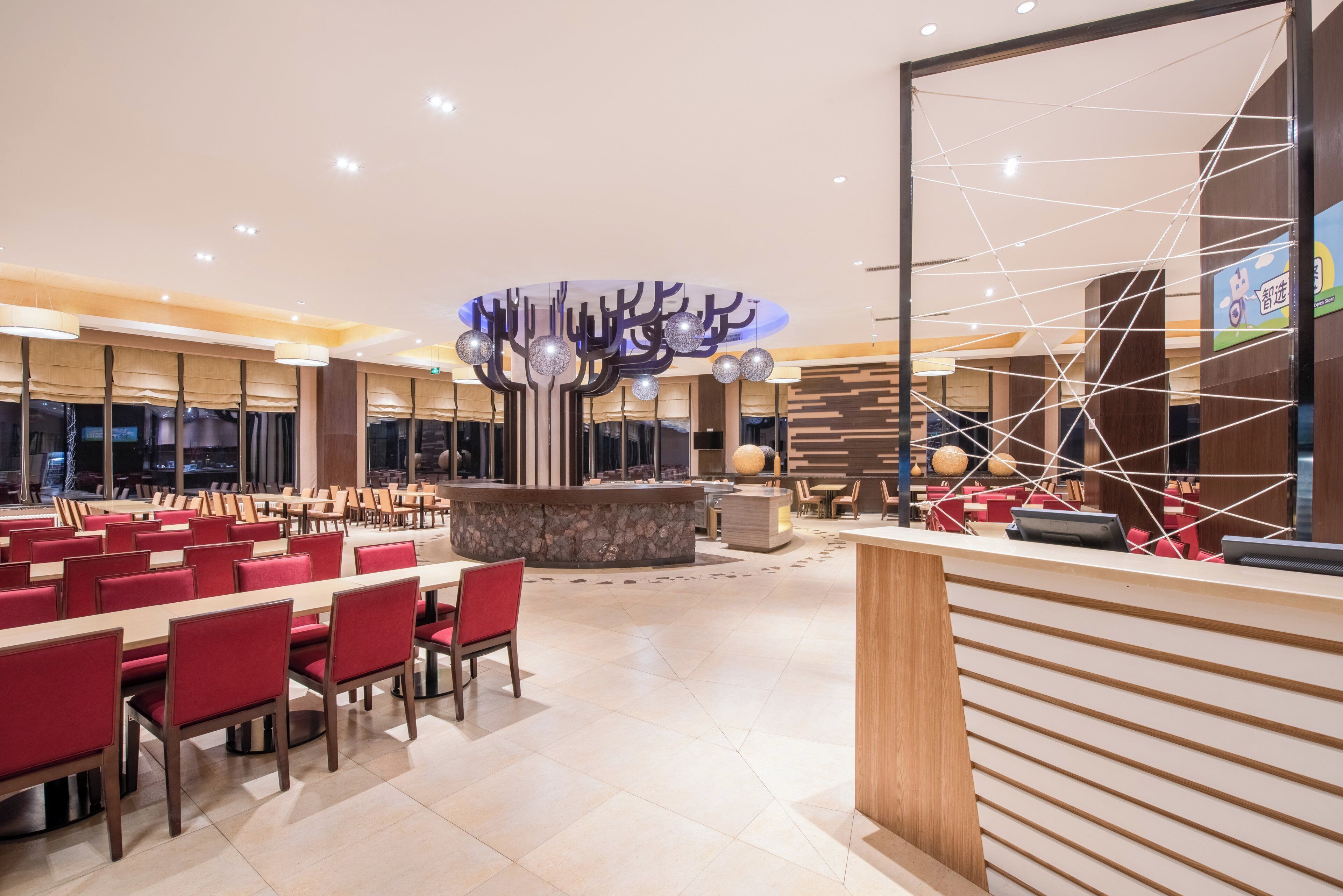 A spacious hotel lobby with a central reception desk, multiple seating areas, and a decorative ceiling feature.