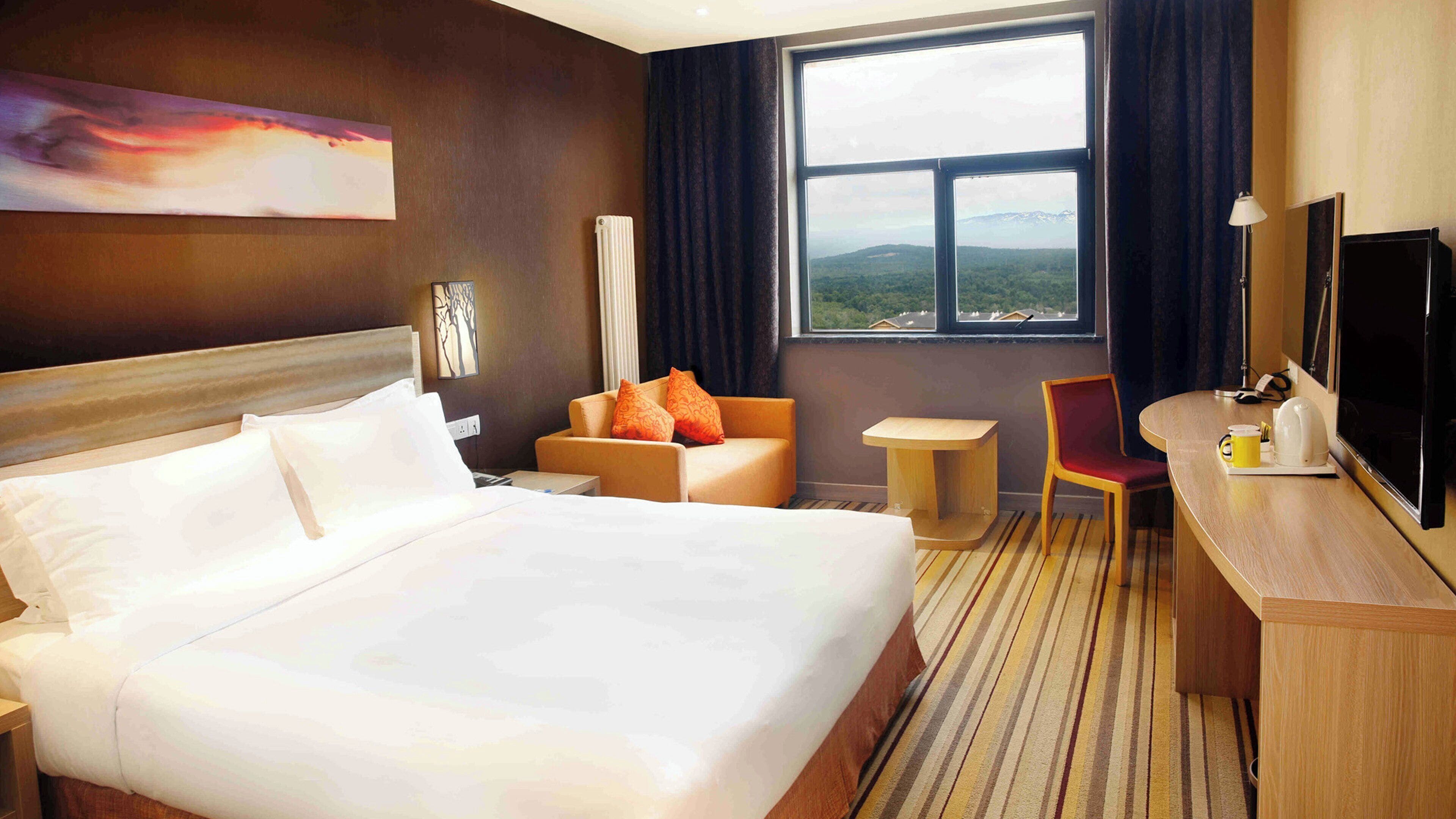 A hotel room with a large bed, a desk, a chair, and a television.