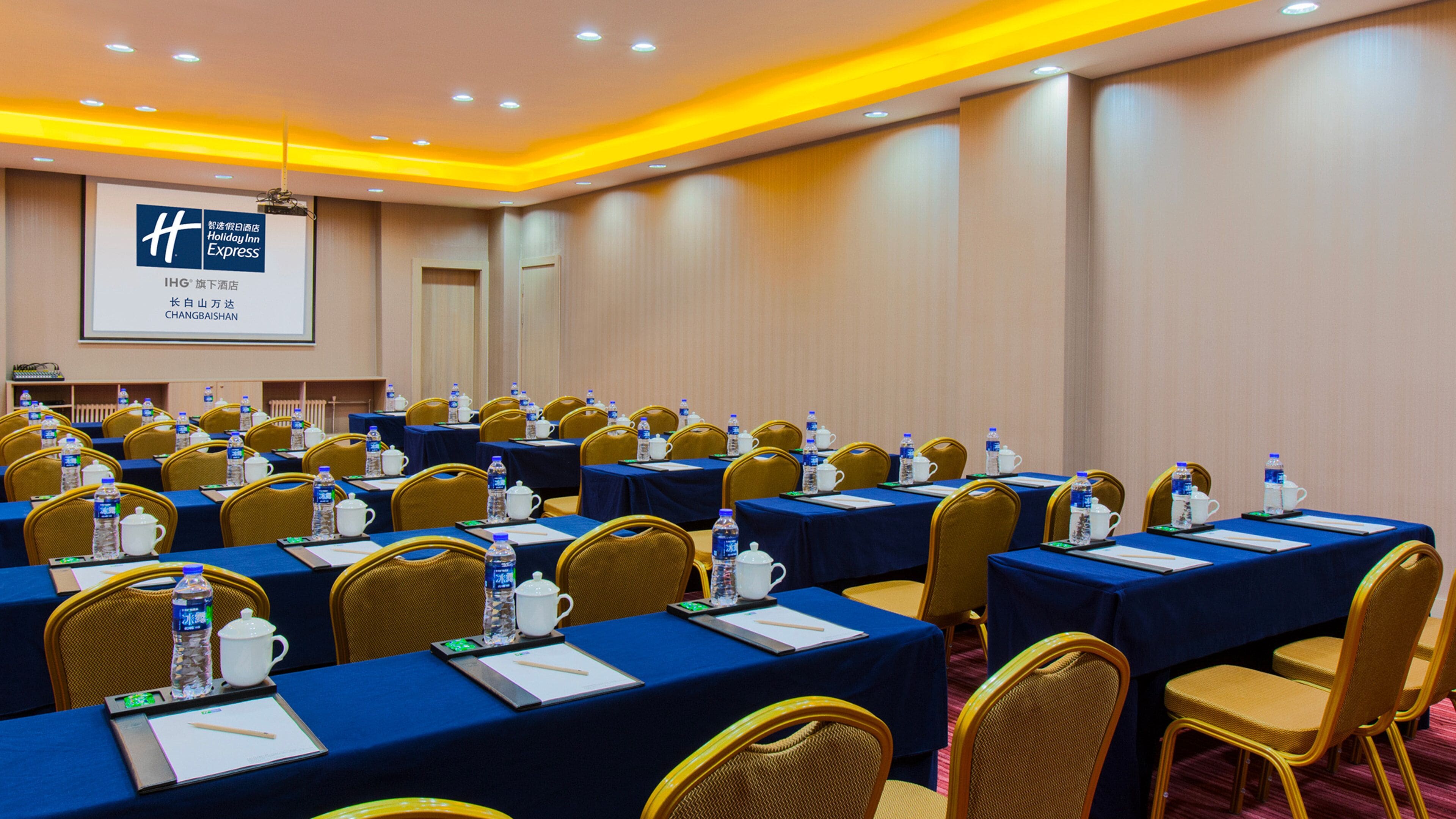 A conference room with rows of tables, chairs, and presentation screens.