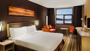 Habitación de hotel con una cama grande, un escritorio, una silla y un ventanal con vistas a un paisaje nevado.