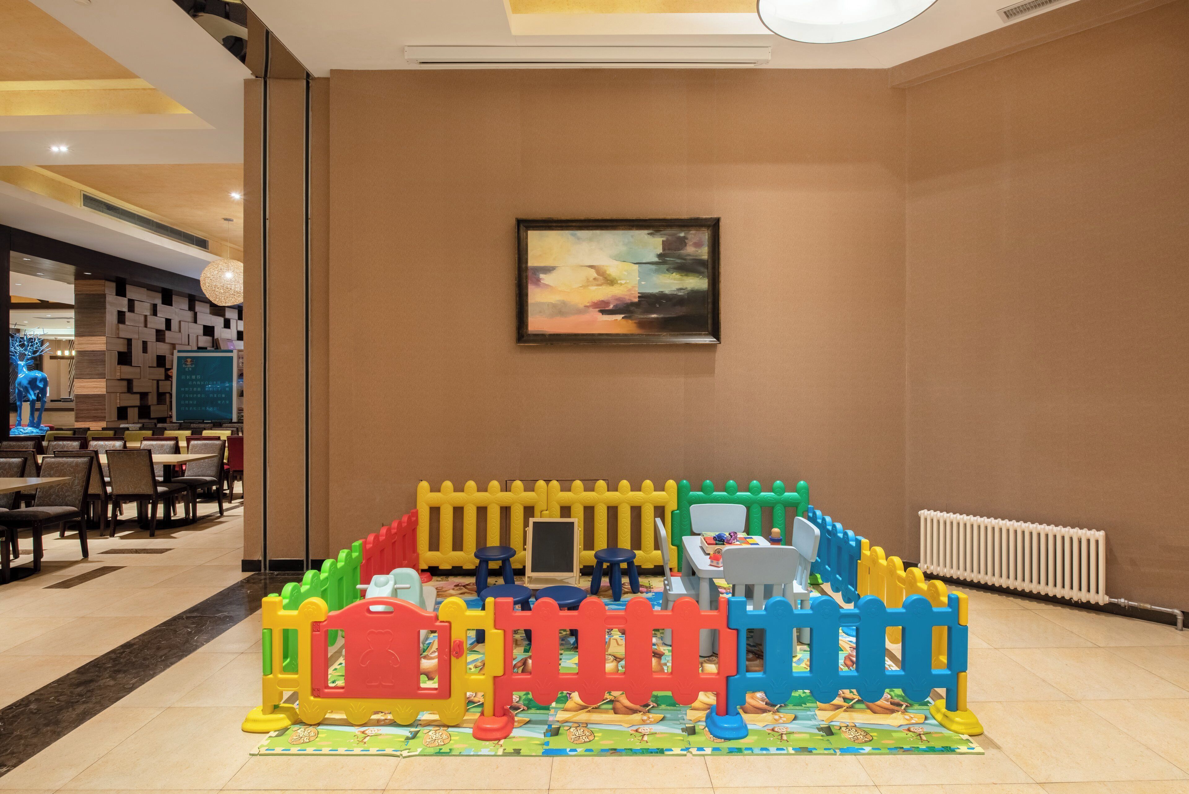 Un espace de jeux pour enfants avec une clôture colorée, une peinture murale et un coin repas en arrière-plan.