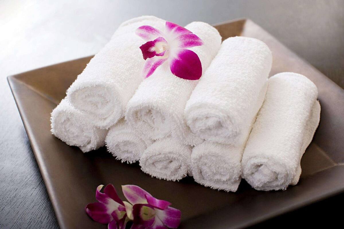 A set of neatly rolled white towels on a square tray with a purple orchid.