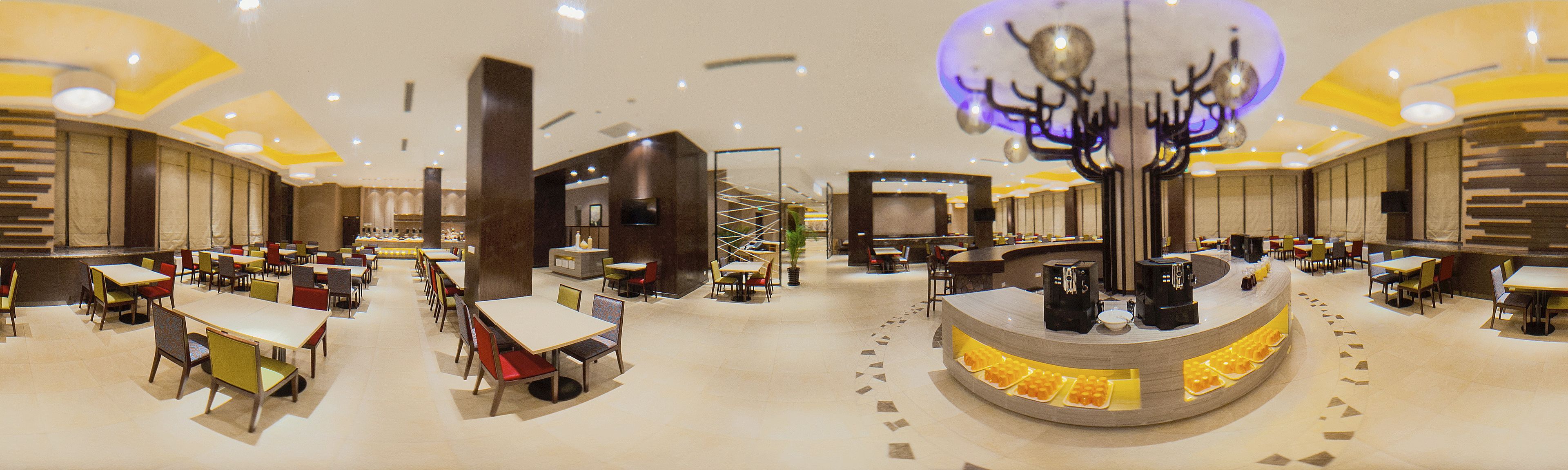 Un hall d’hôtel spacieux, doté de plusieurs espaces salon, d’un bar à café central et d’un élément décoratif au plafond.