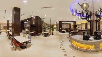 Un hall d’hôtel spacieux, doté de plusieurs espaces salon, d’un bar à café central et d’un élément décoratif au plafond.